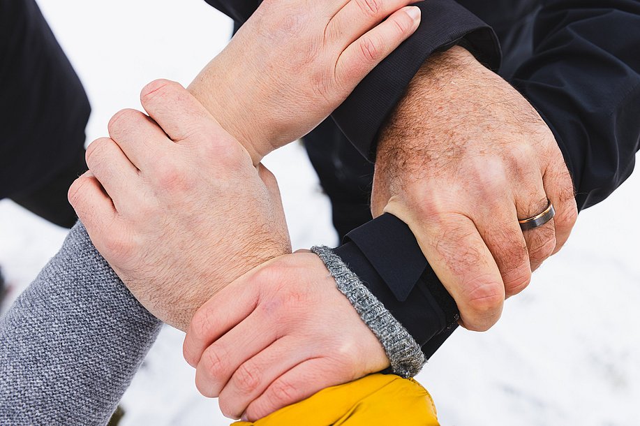 Vier Hände halten sich gegenseitig an den Handgelenken, sodass ein Kreis entsteht