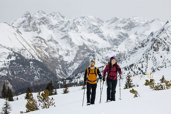 Mann und Frau beim Schneeschuhwandern, im Hintergrund hohe Berge