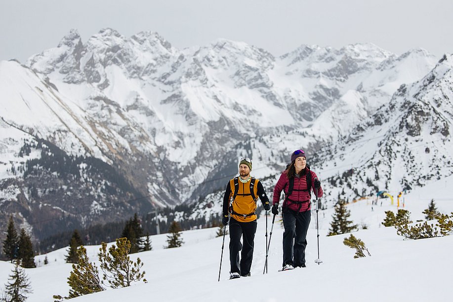 Mann und Frau beim Schneeschuhwandern, im Hintergrund hohe Berge
