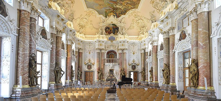 Prachtvoller Kaisersaal der Benediktinerabtei Ottobeuren, bestuhlt, vorne steht ein Flügel