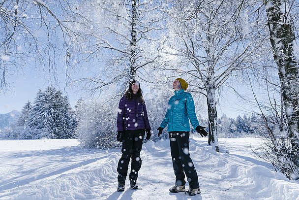 Zwei Frauen auf Winterwanderweg in verschneiter Landschaft
