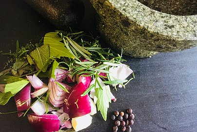 Geschnittene rote Zwiebeln und Kräuter, daneben Pfefferkörner und ein Steinmörser