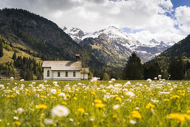 Kapelle in Birgsau auf Blumenwiese mit Bergen mit beschneiten Berggipfeln im Hintergrund
