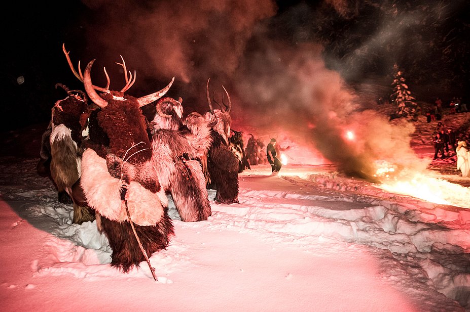 Als Klausen verkleidete Männer stehen im Schnee neben einem Feuer