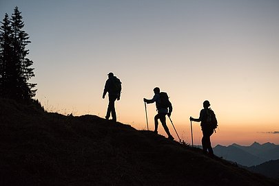 Die Umrisse dreier Wanderer, im Hintergrund der Sonnenaufgang