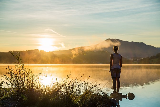 Frau steht bei Sonnenuntergang am See 