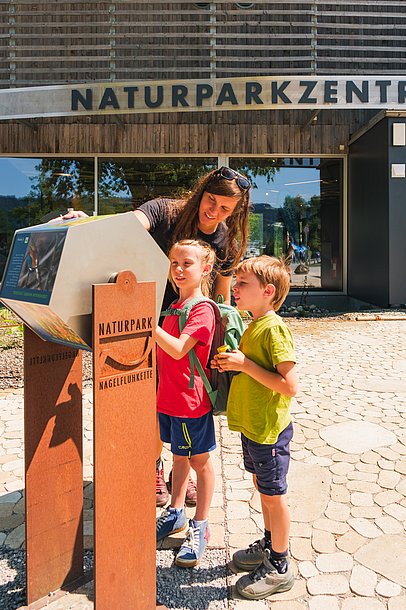 Mutter mit zwei Kindern an einer Erlebnisstation vor dem Naturparkzentrum Nagelfluhkette