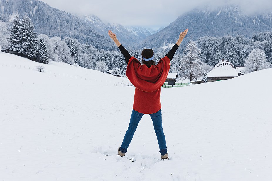 Silvia Fink-Eisinger von hinten in einer Schneelandschaft, die Beine hüftbreit, die Arme zu einem V erhoben