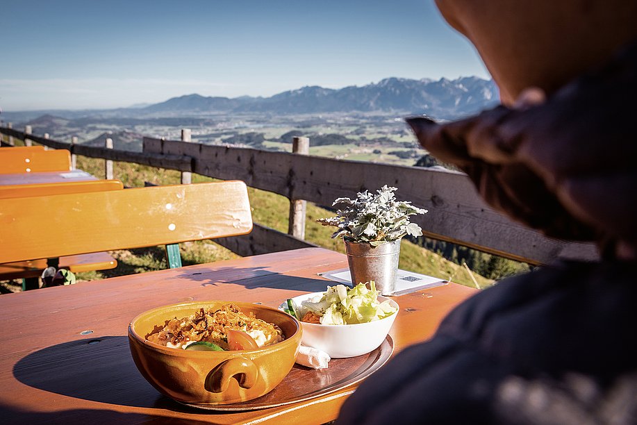 Wanderin auf Terrasse einer Berghütte, mit Kässpatzn und Aussicht