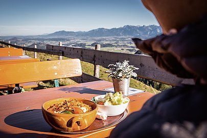 Wanderin auf Terrasse einer Berghütte, mit Kässpatzn und Aussicht