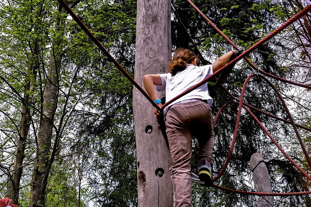 Kind klettert auf Klettergerüst im Wald
