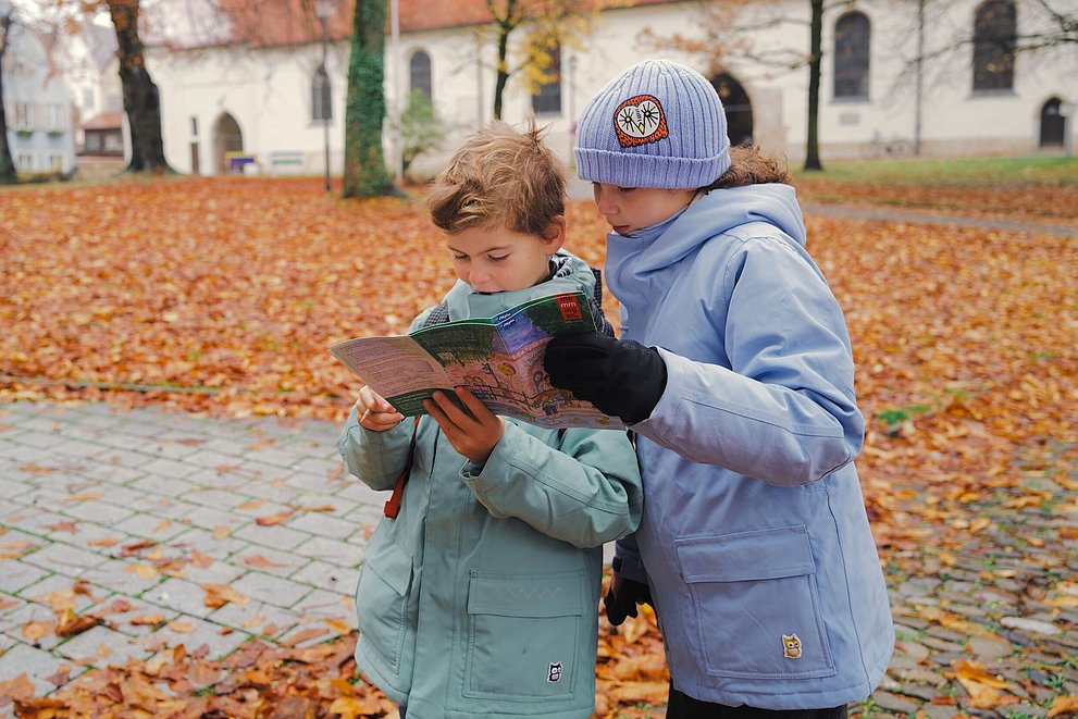 Zwei Kinder schauen in einem herbstlichen Park in ein Prospekt