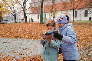 Zwei Kinder schauen in einem herbstlichen Park in ein Prospekt