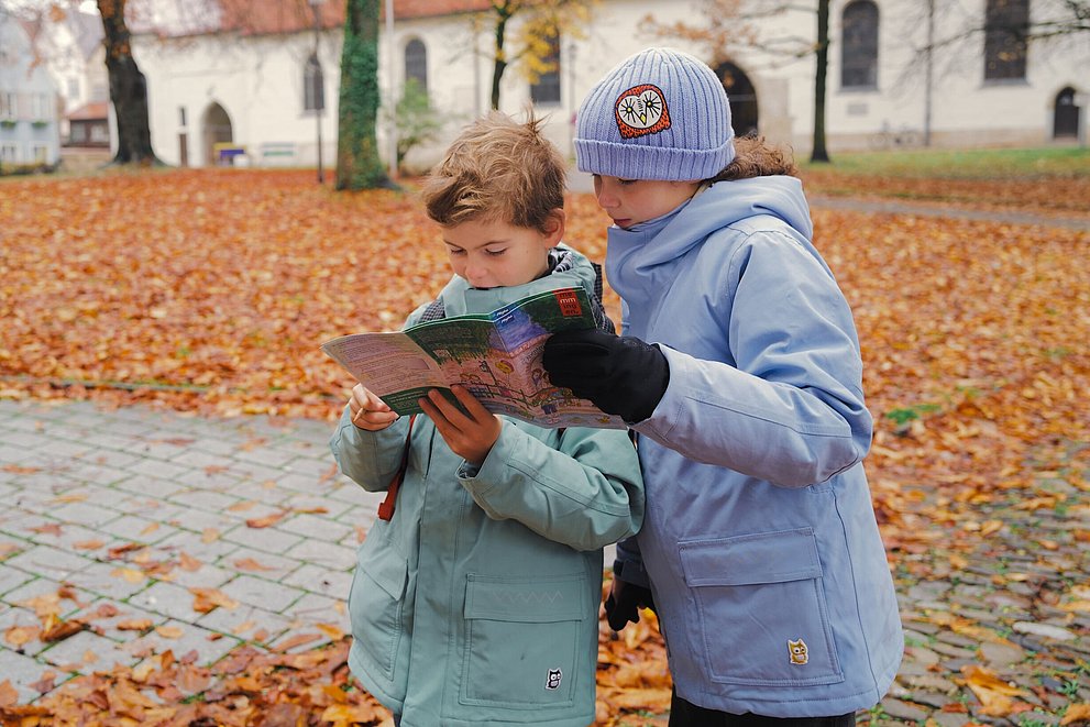 Zwei Kinder schauen in einem herbstlichen Park in ein Prospekt