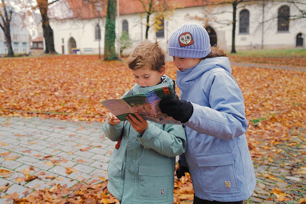 Zwei Kinder schauen in einem herbstlichen Park in ein Prospekt