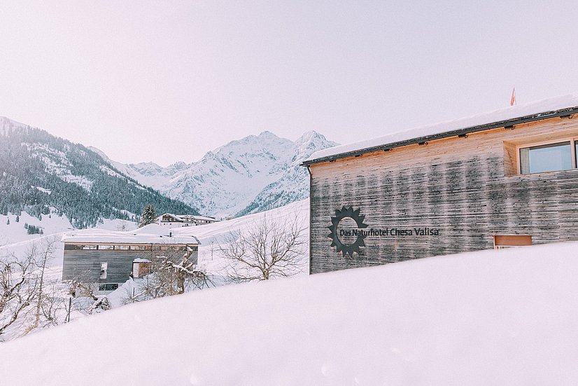 Naturhotel Chesa Valisa mit Holzfassade in Schneelandschaft vor Bergen