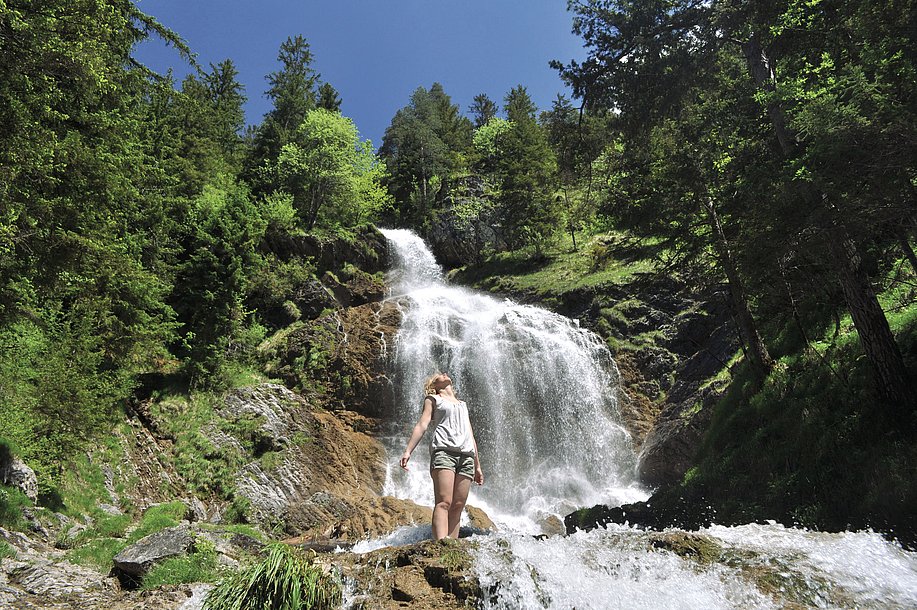 Frau vor Wasserfall blickt zum Himmel