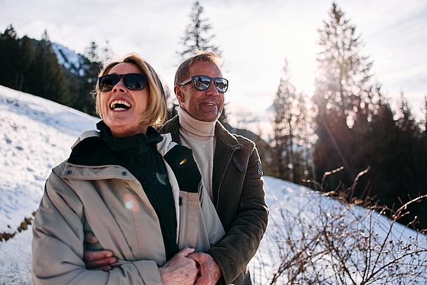 Paar mit Sonnenbrillen Arm in Arm beim Winterwandern Paar mit Sonnenbrillen Arm in Arm beim Winterwandern