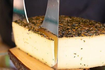 Ein Käselaib wird aufgeschnitten, die Rinde ist mit getrockneten Kräutern und Blüten bedeckt Ein Käselaib wird aufgeschnitten, die Rinde ist mit getrockneten Kräutern und Blüten bedeckt