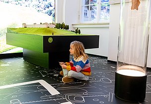 Kind mit Rästelscheibe in der Hand sitzt am Boden im Stadtmuseum Isny