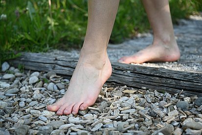 Nackte Füße gehen auf Schotter und Holzschnitzeln