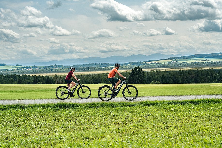 Frau und Mann radeln durch Voralpenlandschaft oberhalb des Wurzacher Beckens