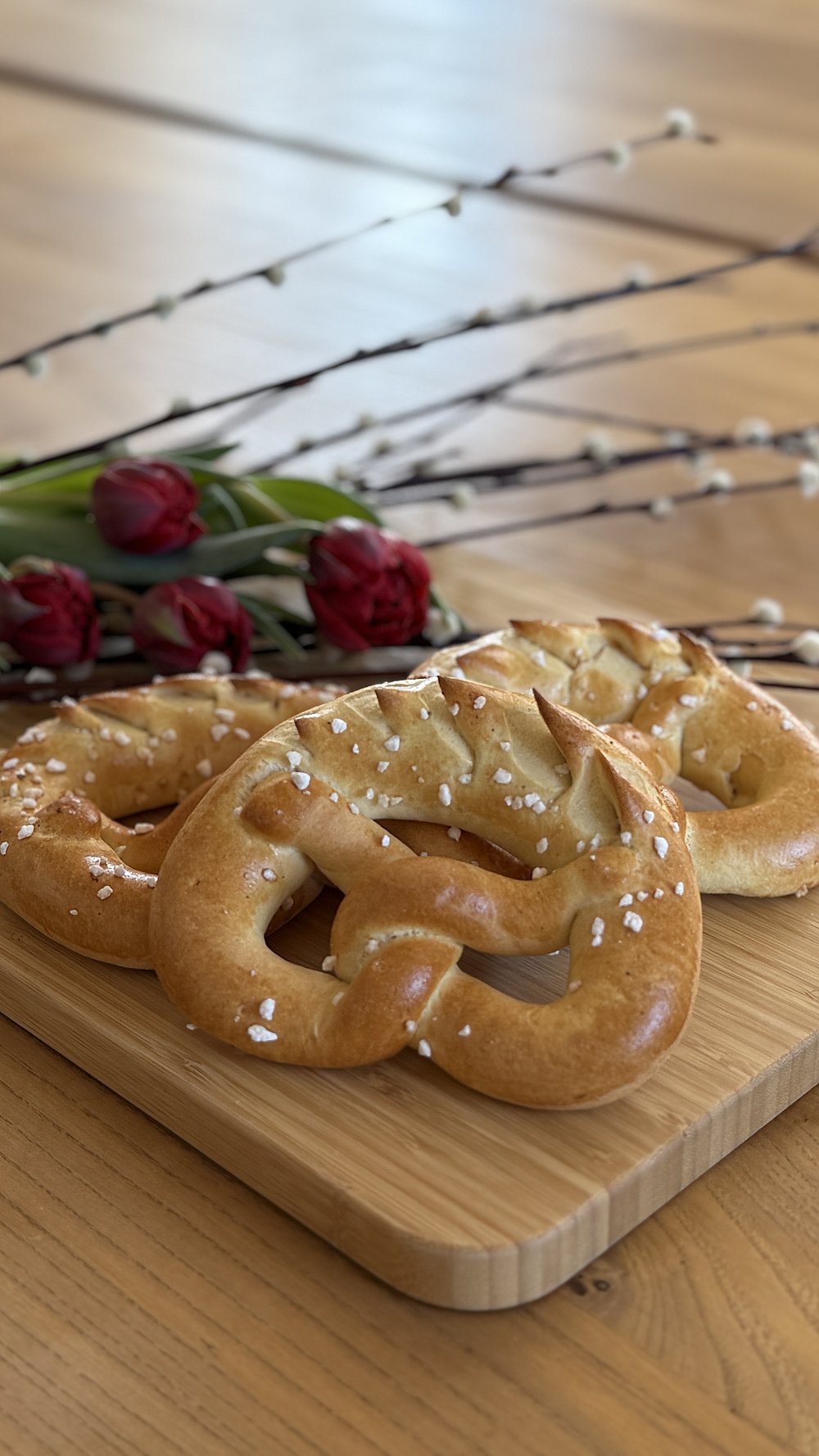 Palmbrezen mit Zucker bestreut auf einem Holzbrett, im Hintergrund Tulpen und Palmzweige