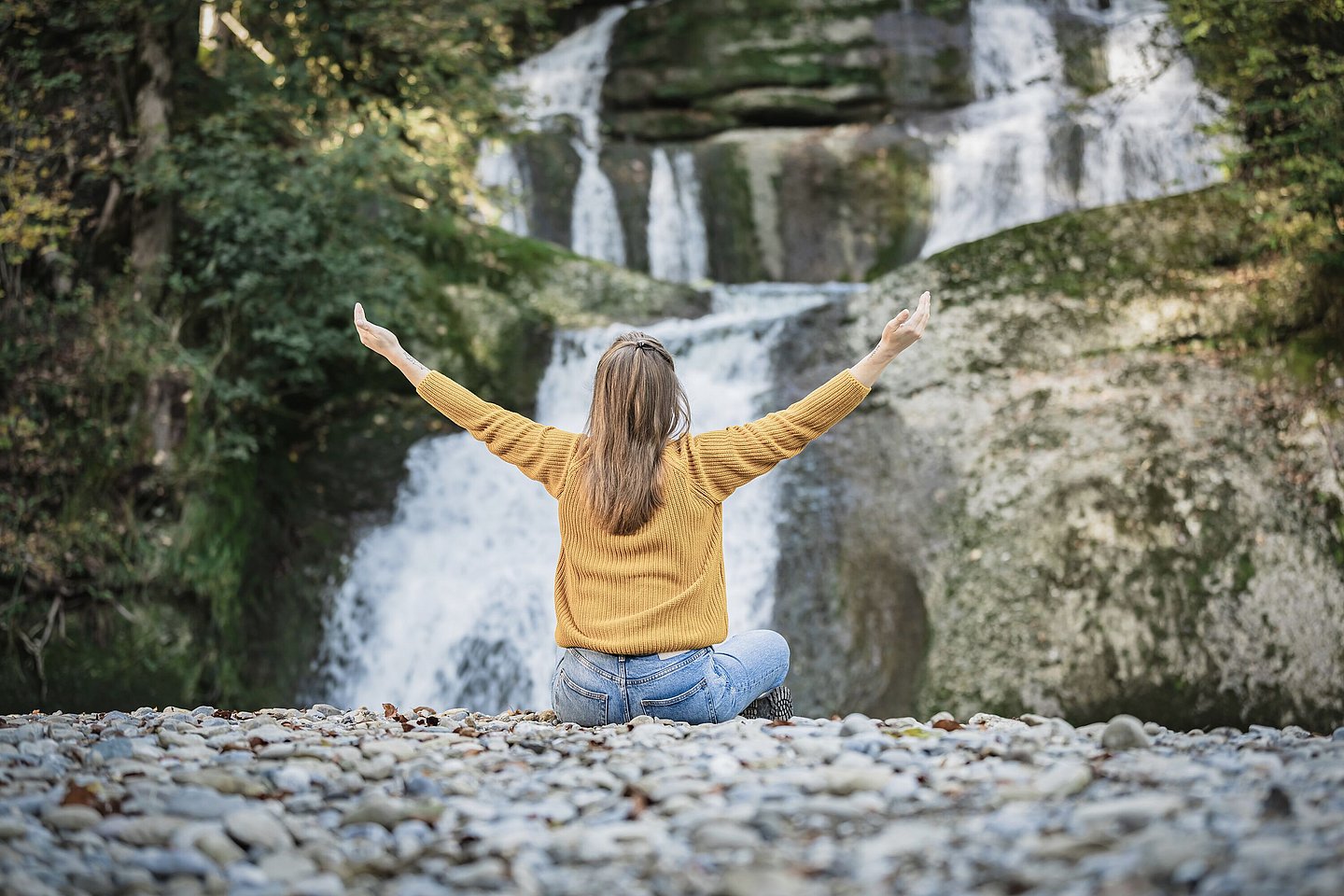 Frau sitzt mit ausgebreiteten Armen vor einem Wasserfall