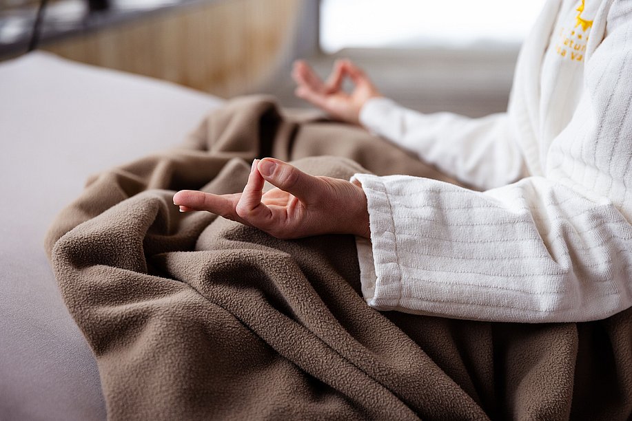 Person in Bademantel im Schneidersitz, Hände in Meditationshaltung Person in Bademantel im Schneidersitz, Hände in Meditationshaltung