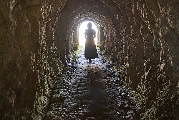 Eine Frau in Tracht von hinten, geht durch eine Höhle