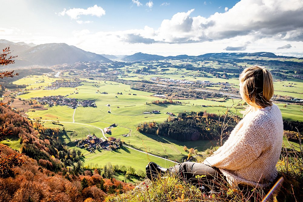 Frau sitzt auf einem Aussichtspunkt und blickt über das Illertal