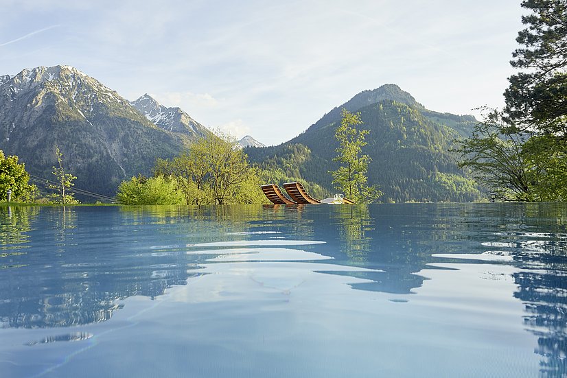 Infinity Pool, dahinter zwei Holzliegen und die Berge