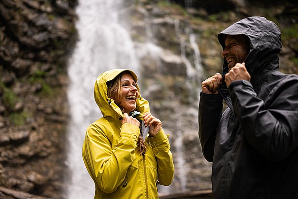 Frau und Mann mit Regenjacken vor einem Wasserfall