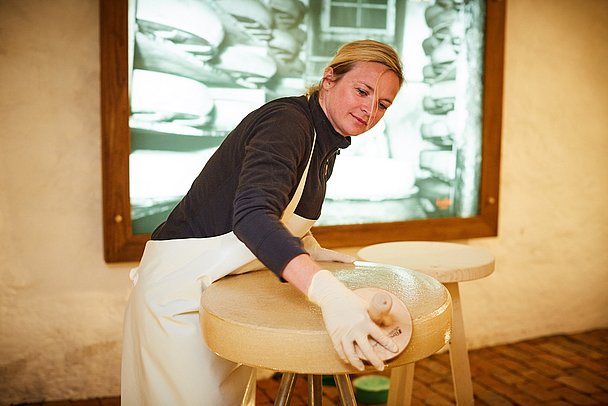 Frau schmiert einen großen Laib Käse
