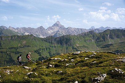 Zwei Wanderer, im Hintergrund ein grüner Grat und felsige Gipfel