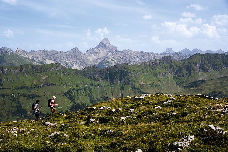 Zwei Wanderer, im Hintergrund ein grüner Grat und felsige Gipfel