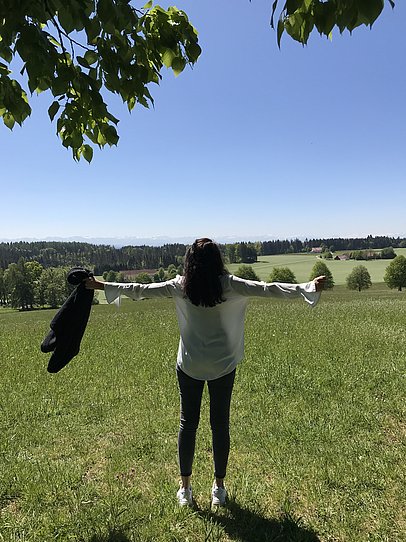 Frau von hinten mit ausgebreiteten Armen auf einer Wiese