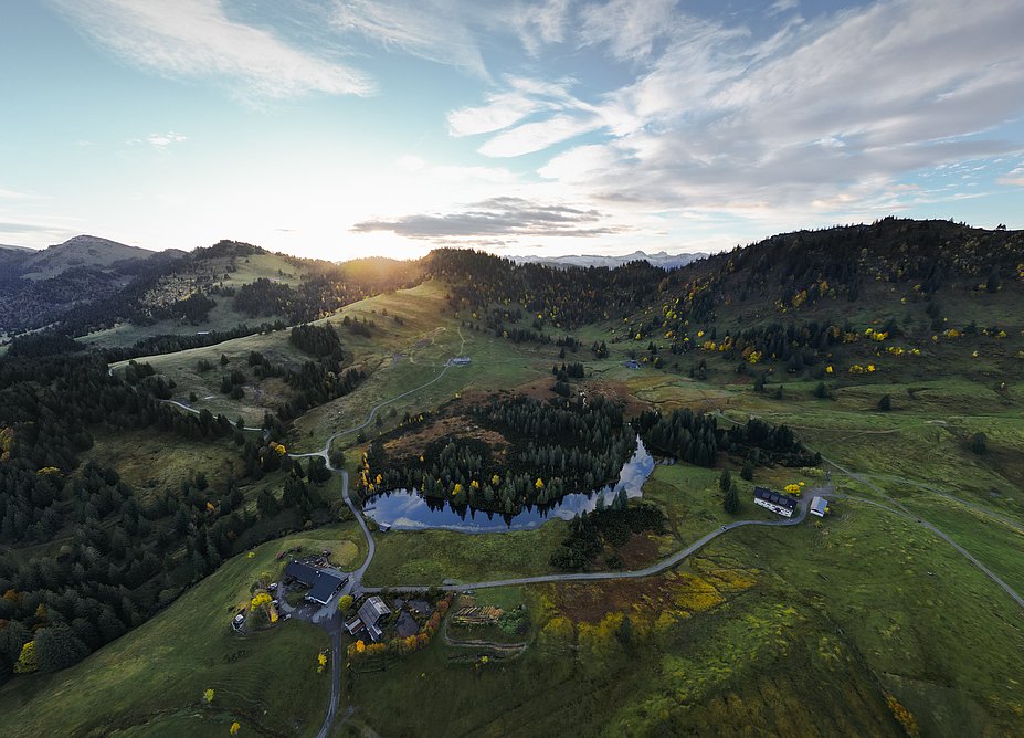 Berglandschaft mit vereinzelten Höfen, Wiesen, Wäldern und See