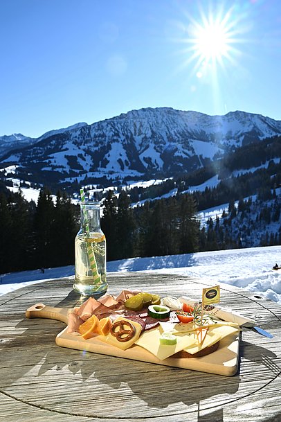 Brotzeit und hausgemachte Limo auf einem Tisch auf der Buchel Alpe vor verschneiten Bergen Brotzeit und hausgemachte Limo auf einem Tisch auf der Buchel Alpe vor verschneiten Bergen