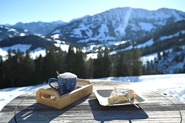 Kaffee und Kuchen auf einem Tisch auf der Buchel Alpe vor verschneiten Bergen Kaffee und Kuchen auf einem Tisch auf der Buchel Alpe vor verschneiten Bergen