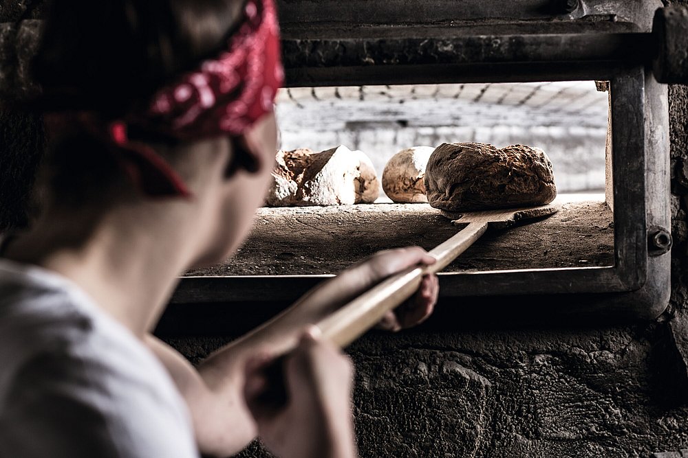 Bäckerin holt ein frisch gebackenes Brot aus einem traditionellen Ofen