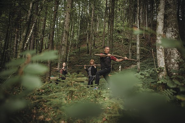 Ein Mann und zwei Frauen machen Sport im Wald mit einem Ast in der Hand