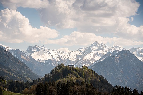 Schöllanger Burgkirche auf einem bewaldeten Hügel, im Hintergrund verschneite Berge Schöllanger Burgkirche auf einem bewaldeten Hügel, im Hintergrund verschneite Berge