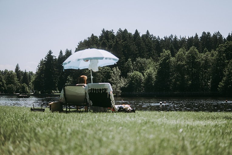 Paar auf Liegestühlen unter einem Sonnenschirm am Waldsee in Lindenberg