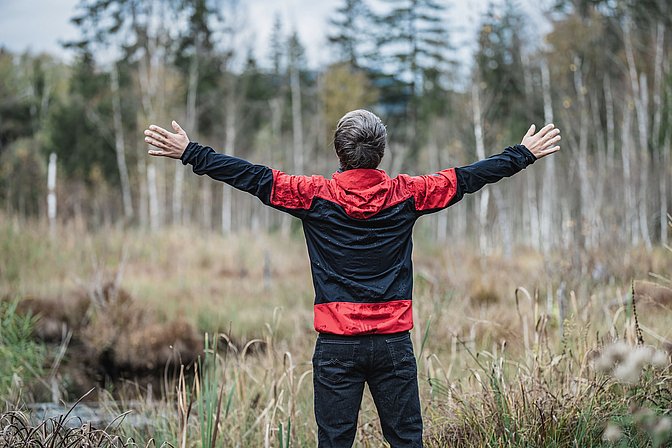 Mann steht im Regen in einer Moorlandschaft und breitet die Arme aus
