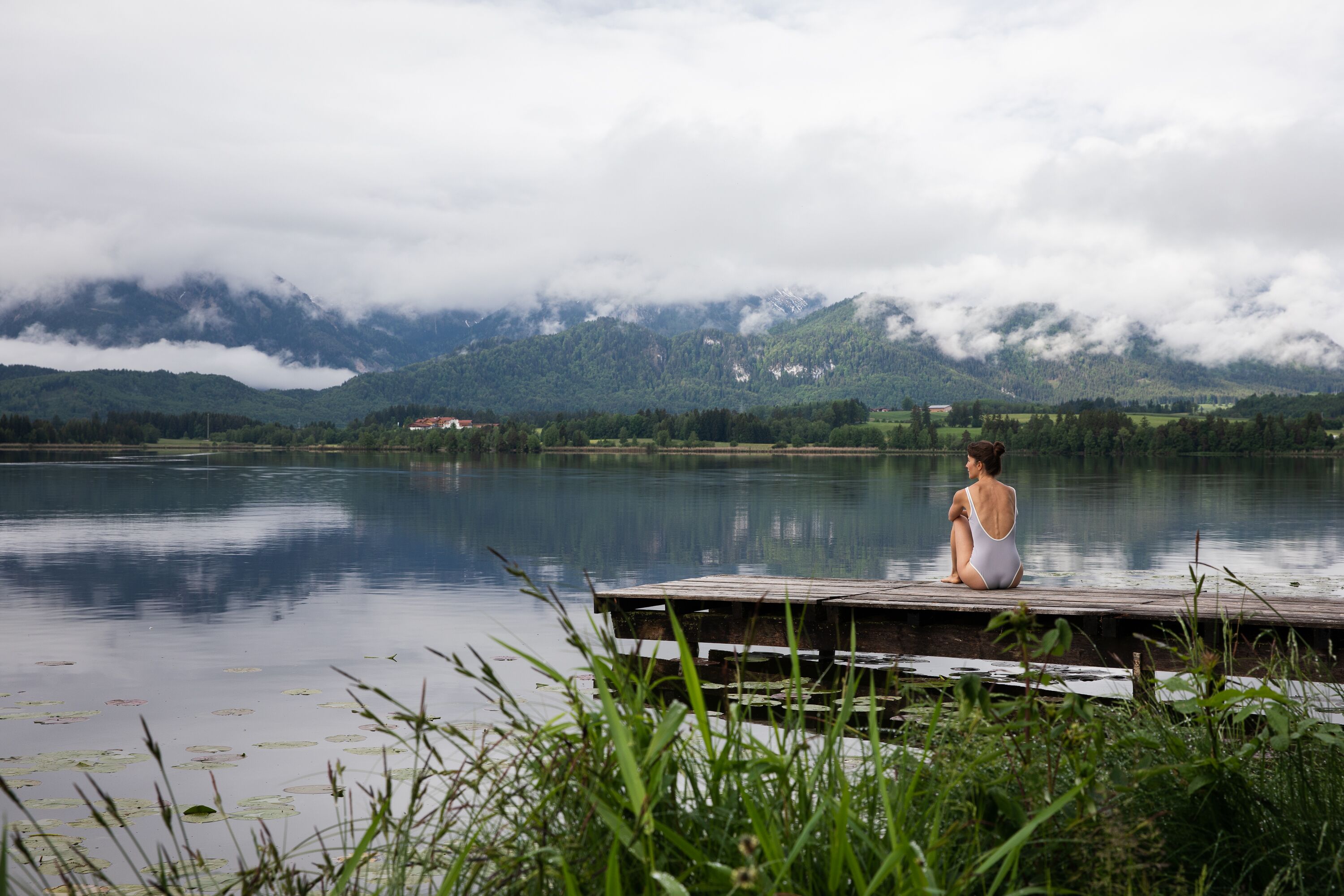 Eine junge Frau sitzt auf einem Steg am See und schaut in die Weite