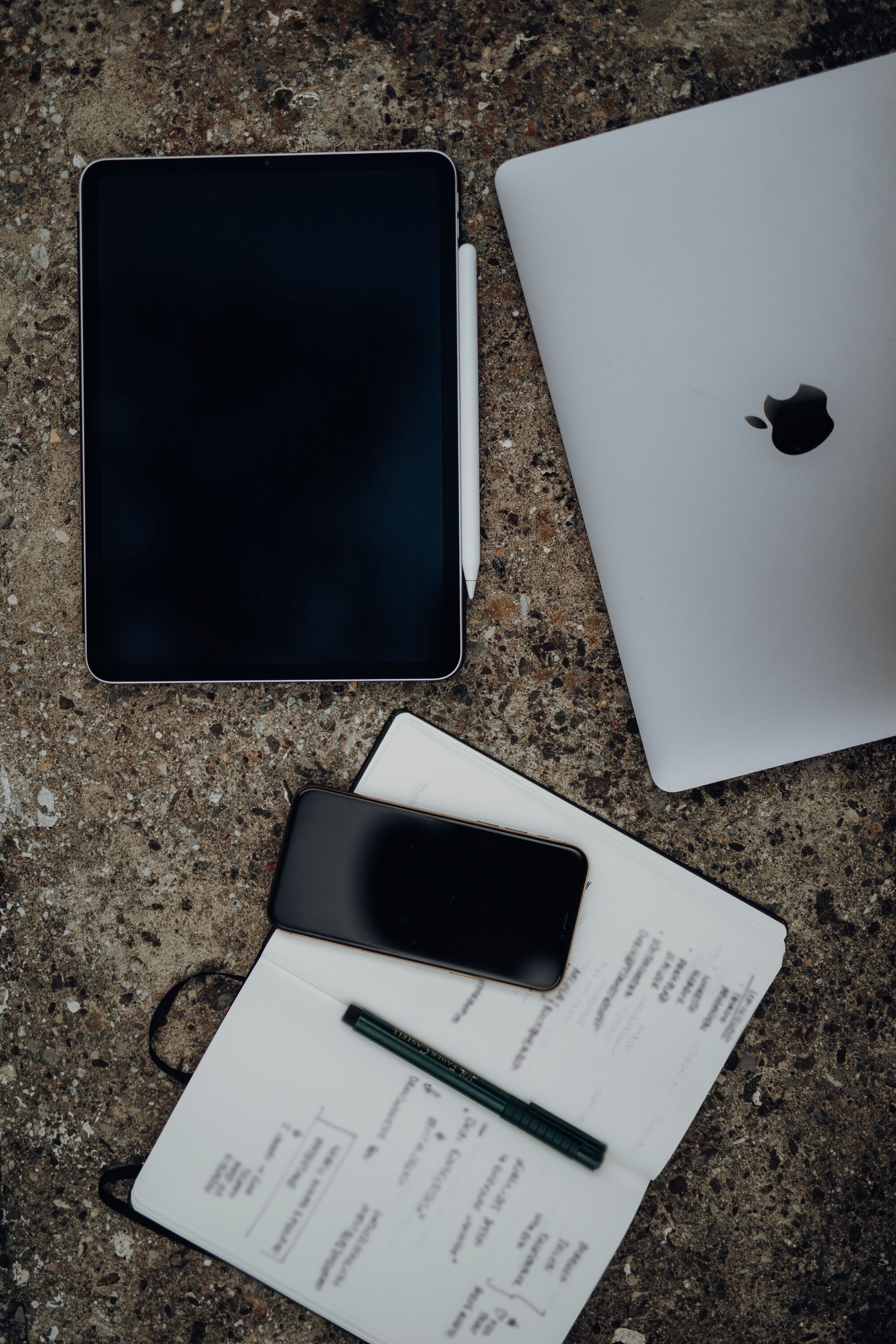 Ein Laptop, Tablet, Notizbuch und Handy liegen auf einem Tisch 
