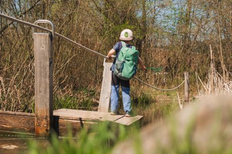 Junge mit Forschurrucksack und Kescher in der Hand auf einem Floß am Alpsee