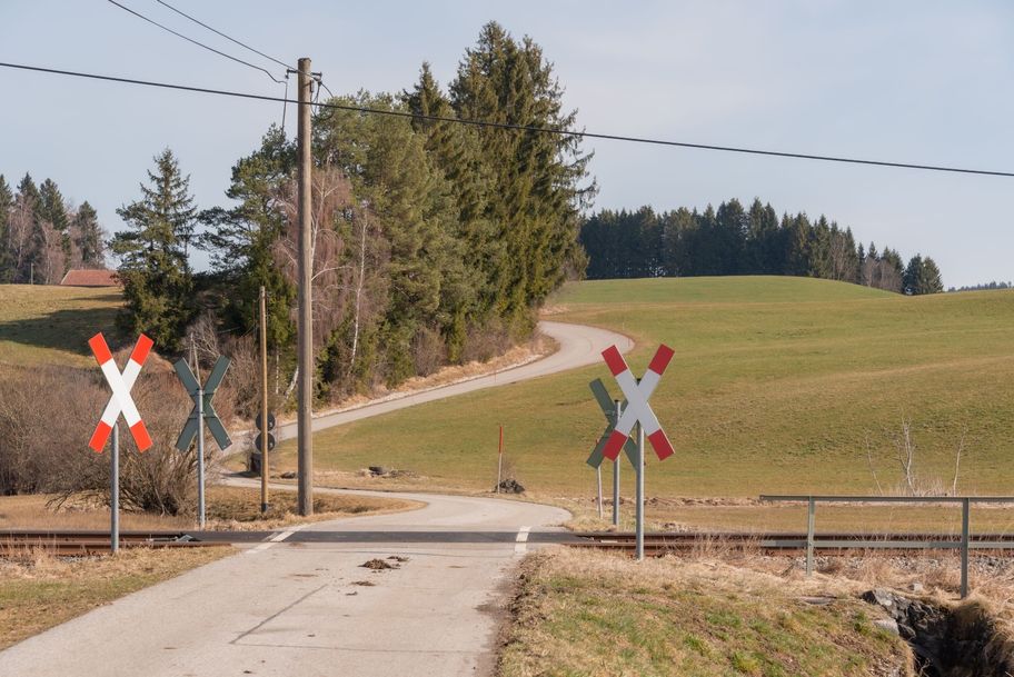 Über einen unbeschrankten Bahnübergang schlängelt sich der Weg am Waldrand entlang über die hügeligen Felder der Voralpenlandschaft.