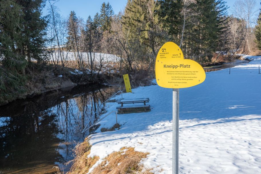 Kneipp-Platz mit Haltestangen im flachen Bachlauf mit Sitzbänken.